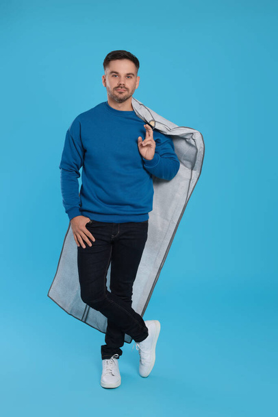 Man holding garment cover with clothes on light blue background. Dry-cleaning service - Фото, зображення