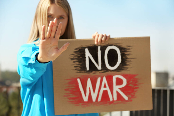 Грустная женщина держит плакат со словами "Нет войне" и показывает стоп-жест на открытом воздухе - Фото, изображение