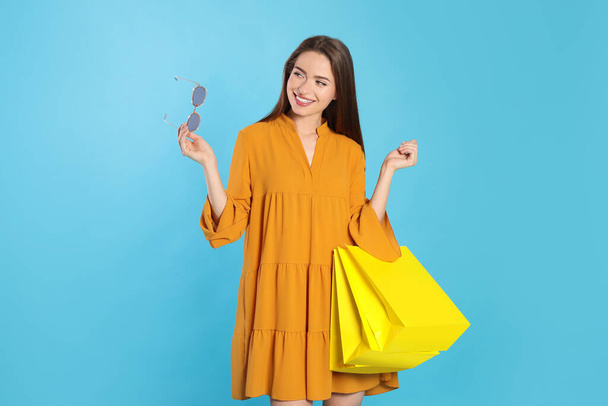Happy young woman with shopping bags on light blue background. Big sale - Фото, изображение