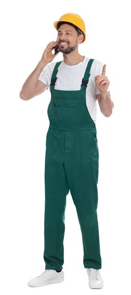 Professional repairman in uniform talking on phone against white background - Photo, image