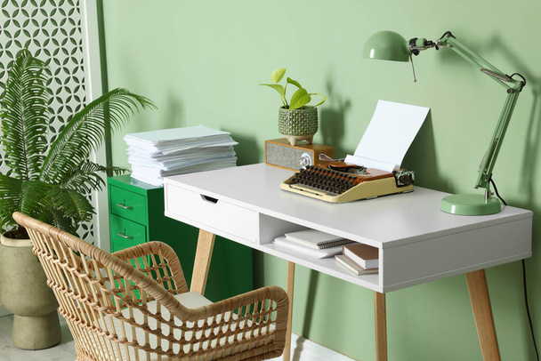 Writer's workplace with typewriter on wooden desk near pale green wall in room - Foto, afbeelding