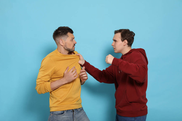 Two emotional men fighting on light blue background - Photo, Image