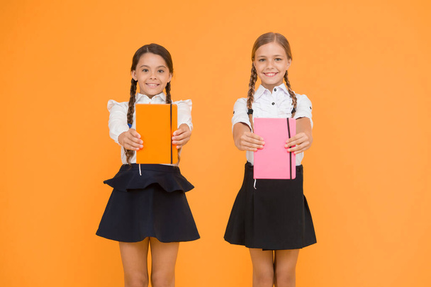 Sharing book love. Happy little girls holding books with colorful covers on yellow background. Cute small children smiling with encyclopedia or hand books. Educational books for pupils and students. - Photo, Image