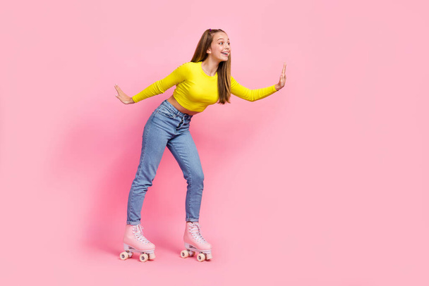 Full length photo of charming excited school girl dressed yellow crop top riding rollers empty space isolated pink color background. - Фото, зображення