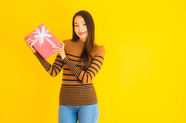 Portrait beautiful young asian woman happy smile with red gift box on yellow isolated background - Photo, Image