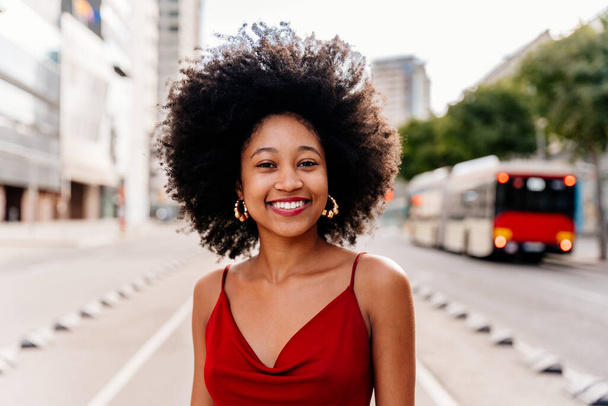 Piękna młoda, szczęśliwa afrykańska kobieta z afro kręconą fryzurą spacerująca po mieście - wesoły czarny student spacerujący po ulicach - Zdjęcie, obraz