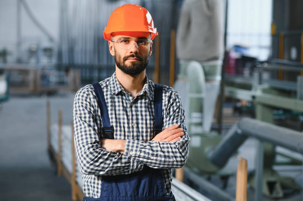 Portrait of Professional Heavy Industry Engineer, Worker Wearing Safety Uniform, Hard Hat Smiling. In the Background Unfocused Large Industrial Factory - Fotó, kép