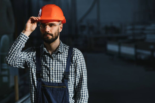 Retrato de engenheiro profissional da indústria pesada, trabalhador vestindo uniforme de segurança, sorriso de chapéu duro. No fundo desfocado grande fábrica industrial - Foto, Imagem