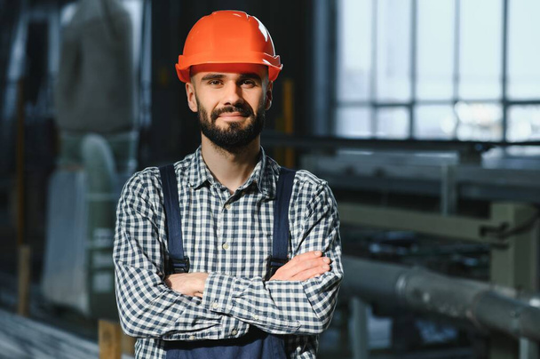 Happy Professional Heavy Industry Engineer Worker Wearing Uniform, and Hard Hat in a Steel Factory. Smiling Industrial Specialist Standing in a Metal Construction Manufacture. - Fotografie, Obrázek