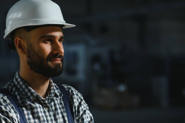 Portrait of Professional Heavy Industry Engineer, Worker Wearing Safety Uniform, Hard Hat Smiling. In the Background Unfocused Large Industrial Factory - Foto, Imagen