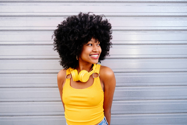 Beautiful young happy african woman with afro curly hairstyle strolling in the city - Cheerful black student portrait on colorful wall background - Photo, image