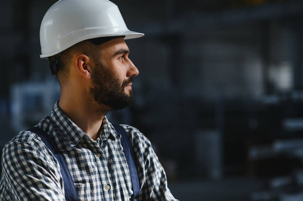 Portrait of Professional Heavy Industry Engineer, Worker Wearing Safety Uniform, Hard Hat Smiling. In the Background Unfocused Large Industrial Factory - Foto, immagini