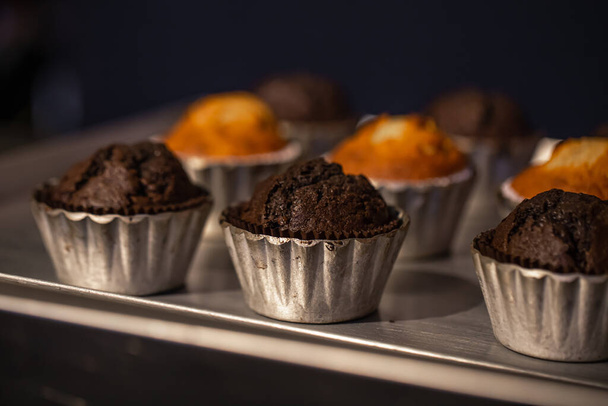 Čerstvě upečené muffiny v kovových formách zblízka v pekárně na tmavém rozmazaném pozadí. - Fotografie, Obrázek