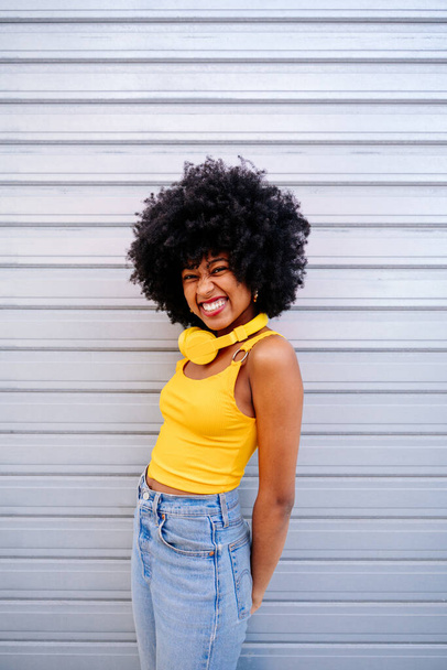 Beautiful young happy african woman with afro curly hairstyle strolling in the city - Cheerful black student portrait on colorful wall background - Foto, Bild