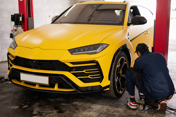 Mechanic checks tire pressure in yellow sport car suv. - Fotografie, Obrázek