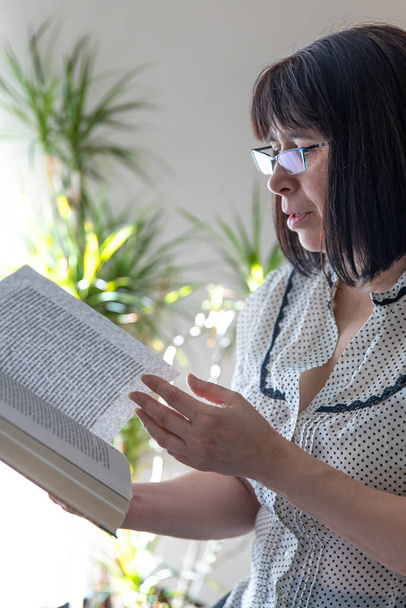 Middelbare leeftijd brunette vrouw met een boek in haar handen in het interieur van het huis. - Foto, afbeelding