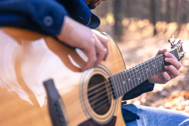 Крупним планом, чоловік грає на акустичній гітарі в лісі в холодну пору року
. - Фото, зображення