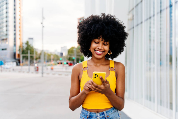 Beautiful young happy african woman with afro curly hairstyle strolling in the city - Cheerful black student girl walking on the street - Фото, зображення