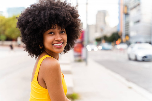 Молодая счастливая африканская женщина с афро-кудрявой прической гуляла по городу - веселая чернокожая студентка шла по улице - Фото, изображение