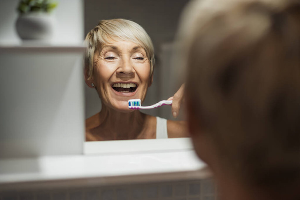 Mature woman is cleaning her teeth in bathroom. - Foto, immagini
