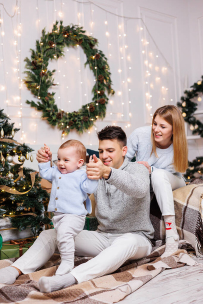 Noel ağacının yanında mutlu bir ailesi olan tatlı bir çocuk. Süslü bir Noel ağacının yakınındaki yatak odasında küçük bir çocuklu bir aile. Şenlikli yeni yıl atmosferi. Aile kutlaması - Fotoğraf, Görsel