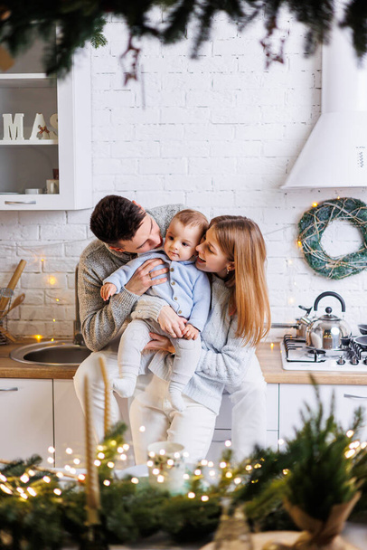 Una familia feliz. Feliz pareja joven con su pequeño hijo en la cocina decorada para el año nuevo. El interior de Año Nuevo en la cocina. Cocina de Navidad. Ambiente familiar festivo. - Foto, imagen