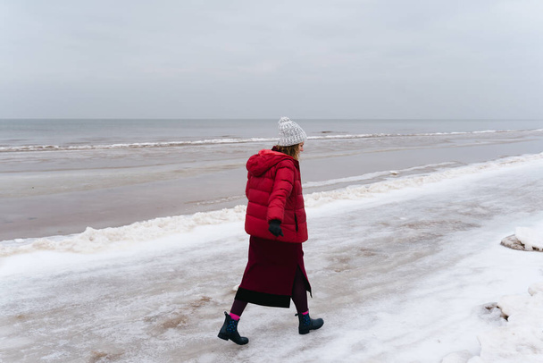 Eine Frau in warmer Kleidung spaziert im Winter am Meer entlang. - Foto, Bild