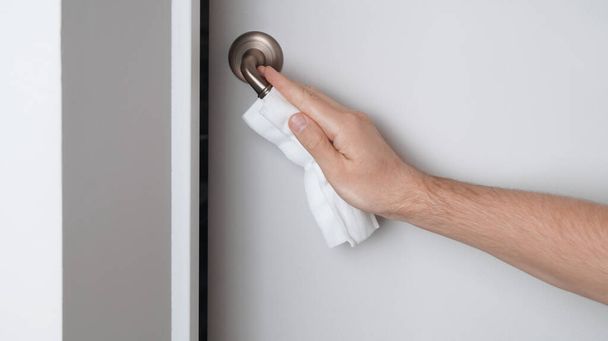 Man cleaning doorknob with wet wipe indoors, closeup. Protective measures - Valokuva, kuva