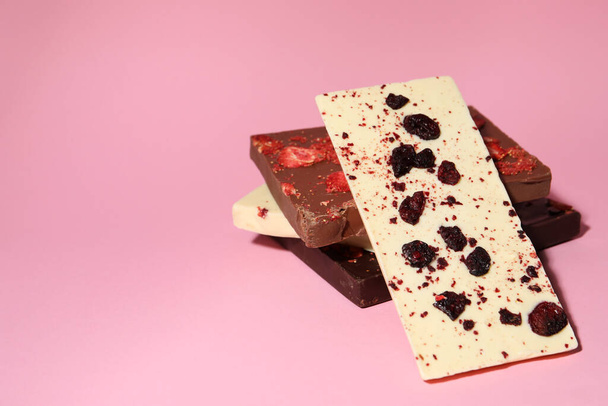 Different chocolate bars with freeze dried fruits on pink background, space for text - Fotó, kép
