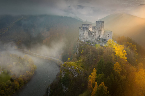 Widok z powietrza na zamek Strecno. Średniowieczny zamek stojący na wysokokalcytowym klifie nad rzeką Wag. Dramatyczny widok zamku w jesiennym górskim krajobrazie, oświetlony promieniami słońca. Pomniki koncepcja, Słowacja. - Zdjęcie, obraz