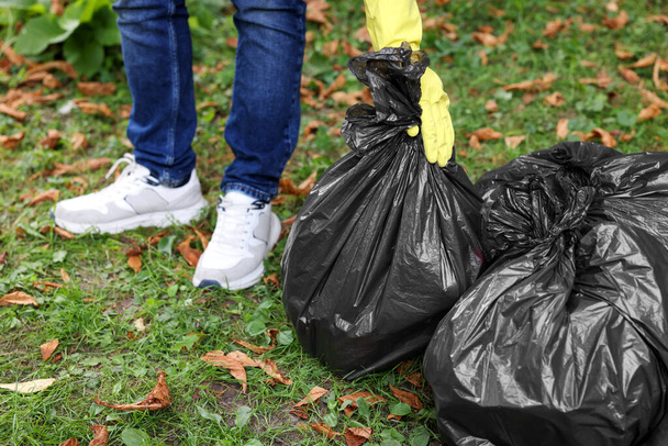 Man holding plastic bags with garbage in park, closeup. - Фото, изображение