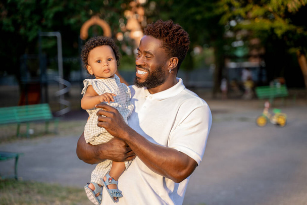 Waist-up portrait of a joyful young man looking at a cute little child in his arms - Fotoğraf, Görsel