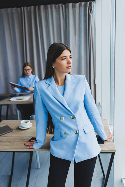オフィスで働いている間、ヨーロッパの実業家。ジャケットを着た若い深刻な千年のブルネットの女性。フリーランスとリモートワークの概念。現代女性のライフスタイル - 写真・画像