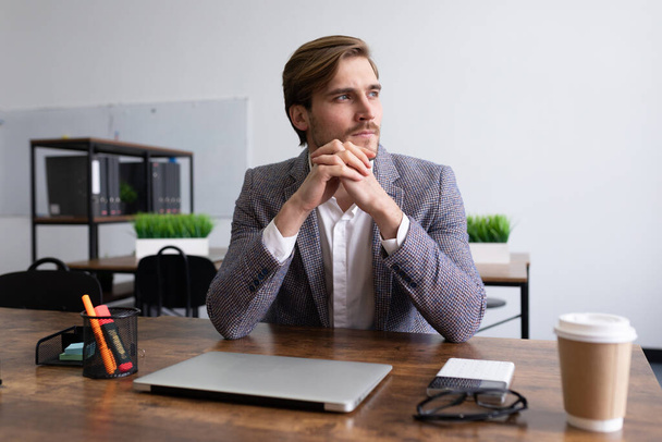 стильный молодой бизнесмен задумчивый сидя за столом в офисе. - Фото, изображение