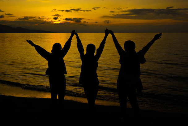 Счастливые и свободные силуэты людей на фоне заката, силуэт трех женщин с поднятыми руками на закате - Фото, изображение
