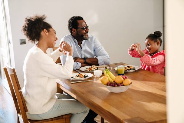 African american family woman and man with little daughter smiling and having breakfast at home - Фото, изображение