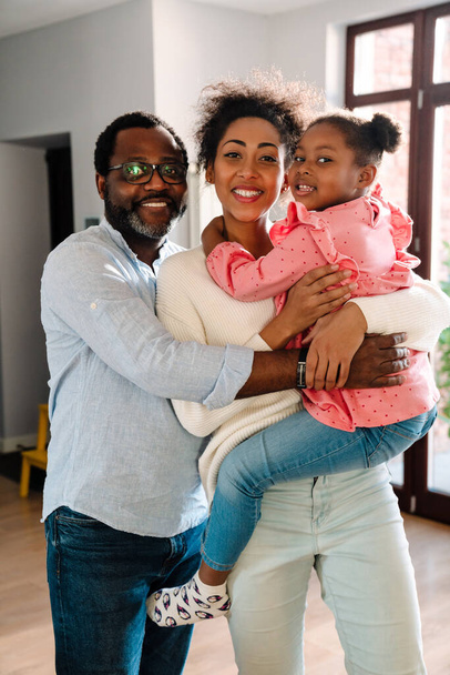 Afričanky americká rodina žena a muž s malou dcerou usmívat a objímání společně doma - Fotografie, Obrázek