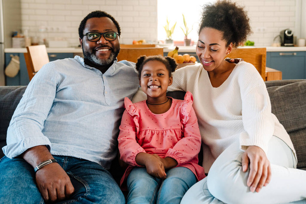 African american family woman and man with little daughter smiling and sitting on sofa at home - Foto, Imagen