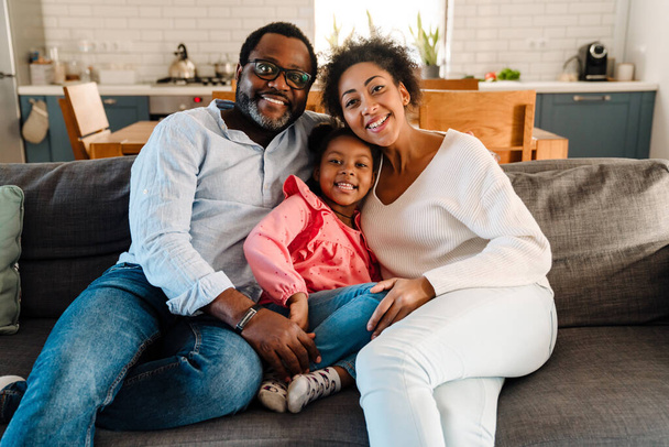 African american family woman and man with little daughter smiling and sitting on sofa at home - Photo, Image