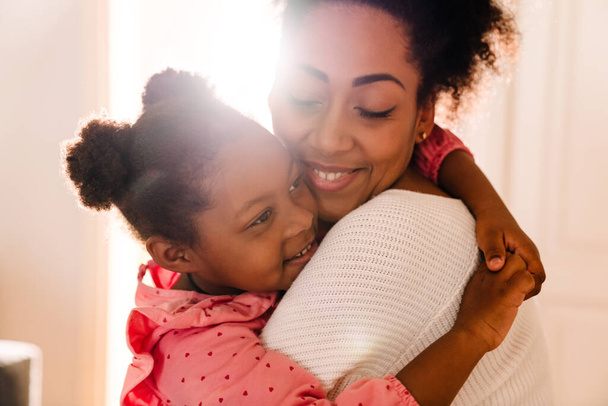 African american happy adult woman smiling and hugging her little daughter at home - Foto, afbeelding
