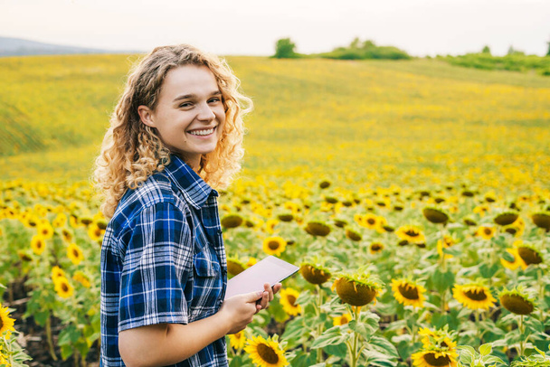 ひまわり畑のデジタルタブレット上のモバイルアプリケーションを使用して、畑で働く幸せな女性農家を笑顔。テキストのための自由なスペース。賢いという概念 - 写真・画像