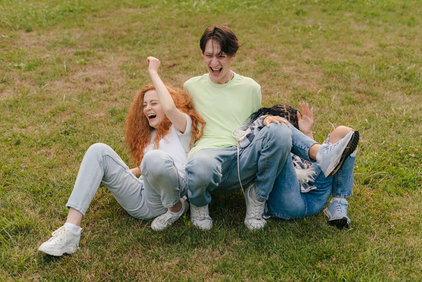 Трое молодых улыбающихся подростков в летней одежде позируют в парке. Позитивные эмоции лица. Happy positive people, group portrait. - Фото, изображение