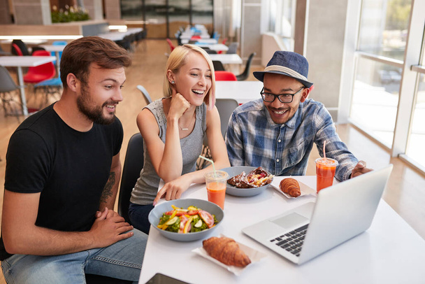 さまざまな男性と女性の上から笑顔とレストランで昼食中にテーブルに座っている間にノートパソコンで面白いビデオを見て - 写真・画像