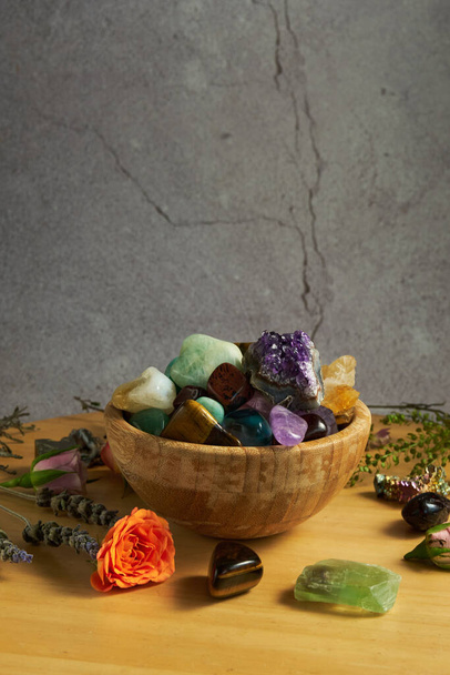 várias pedras preciosas em uma tigela de madeira em um fundo cinza - Foto, Imagem
