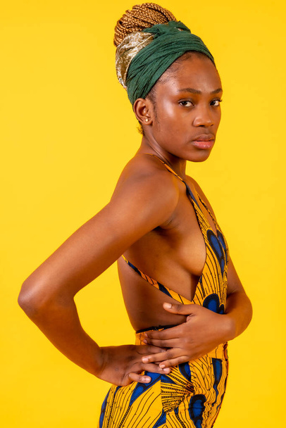 African young woman in the studio on a yellow background, traditional costume, serious look - Фото, изображение