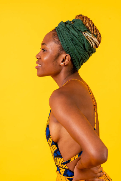One person woman of black ethnicity with traditional costume on yellow background, model in profile smiling - Fotografie, Obrázek