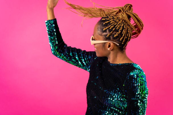 African young woman with party braids on a pink background, smiling dancing and looking - Фото, изображение