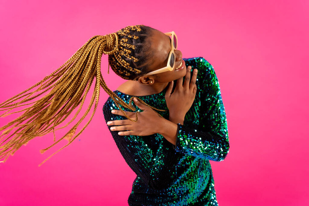 African young woman with party braids on a pink background, having fun dancing moving her hair - Φωτογραφία, εικόνα