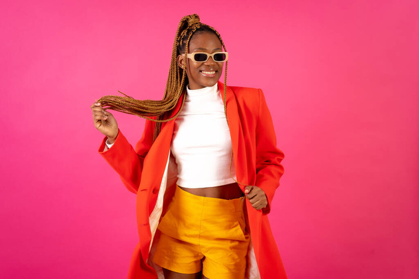 African young woman with braids on a pink background, portrait in a red suit and yellow pants - Photo, Image