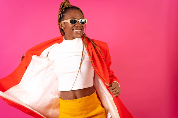 Black ethnic woman with braids on a pink background, portrait in a red outfit having fun - Fotó, kép